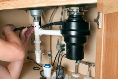 Plumber repairing a garbage disposal beneath a kitchen sink in Bonita Springs